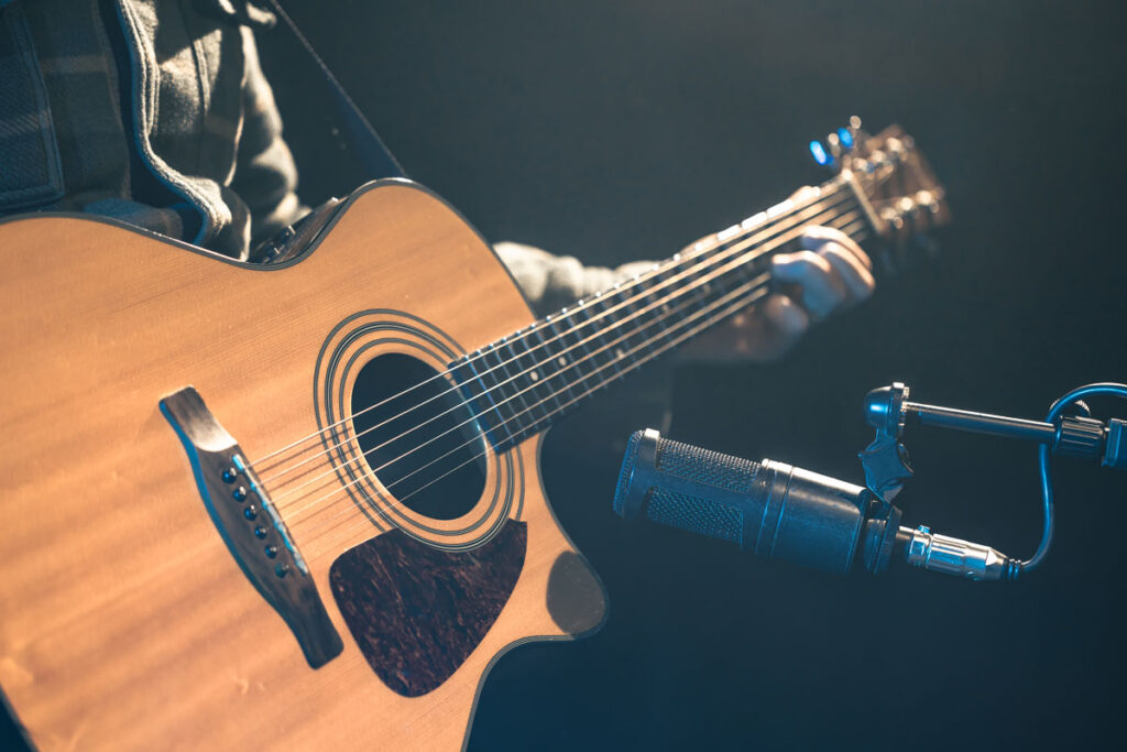 Male-musician-playing-acoustic-guitar-behind-microphone