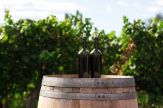 Two wine bottles sitting on top of a wine barrel.