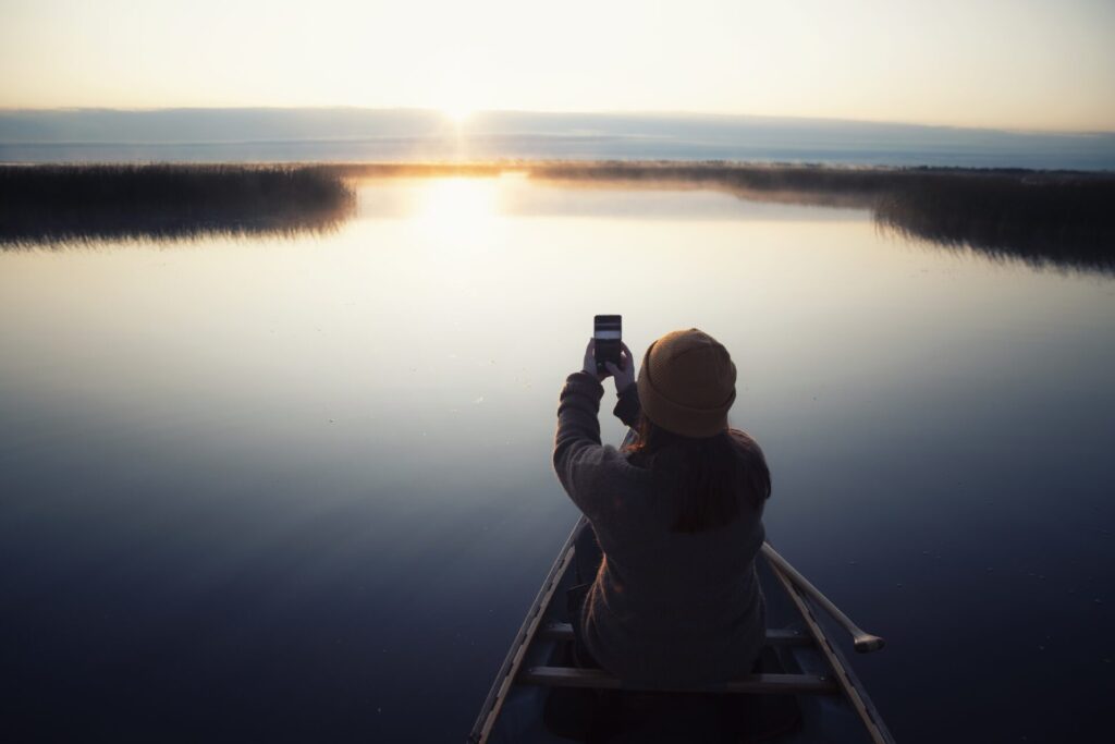 Woman in a canoe taking a picture of the midnight sun